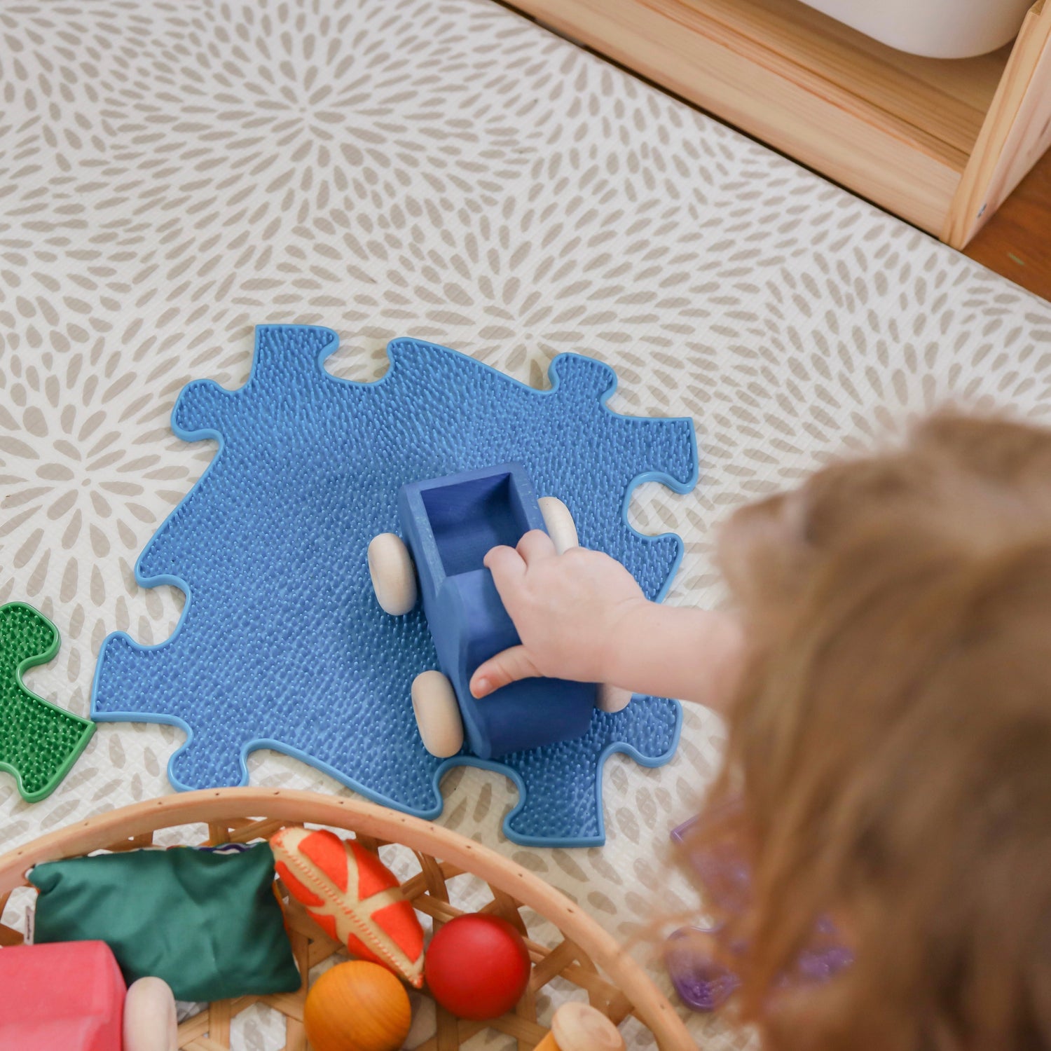 boy playing with a blue car on a blue sensory mat whic is open ended toys for children from tinnitots