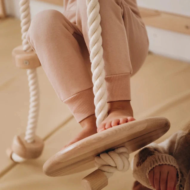 Child's feet on a wooden swing with pink pants