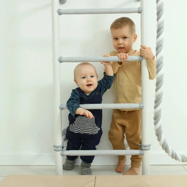 Two children climbing a white ladder against a white wall.