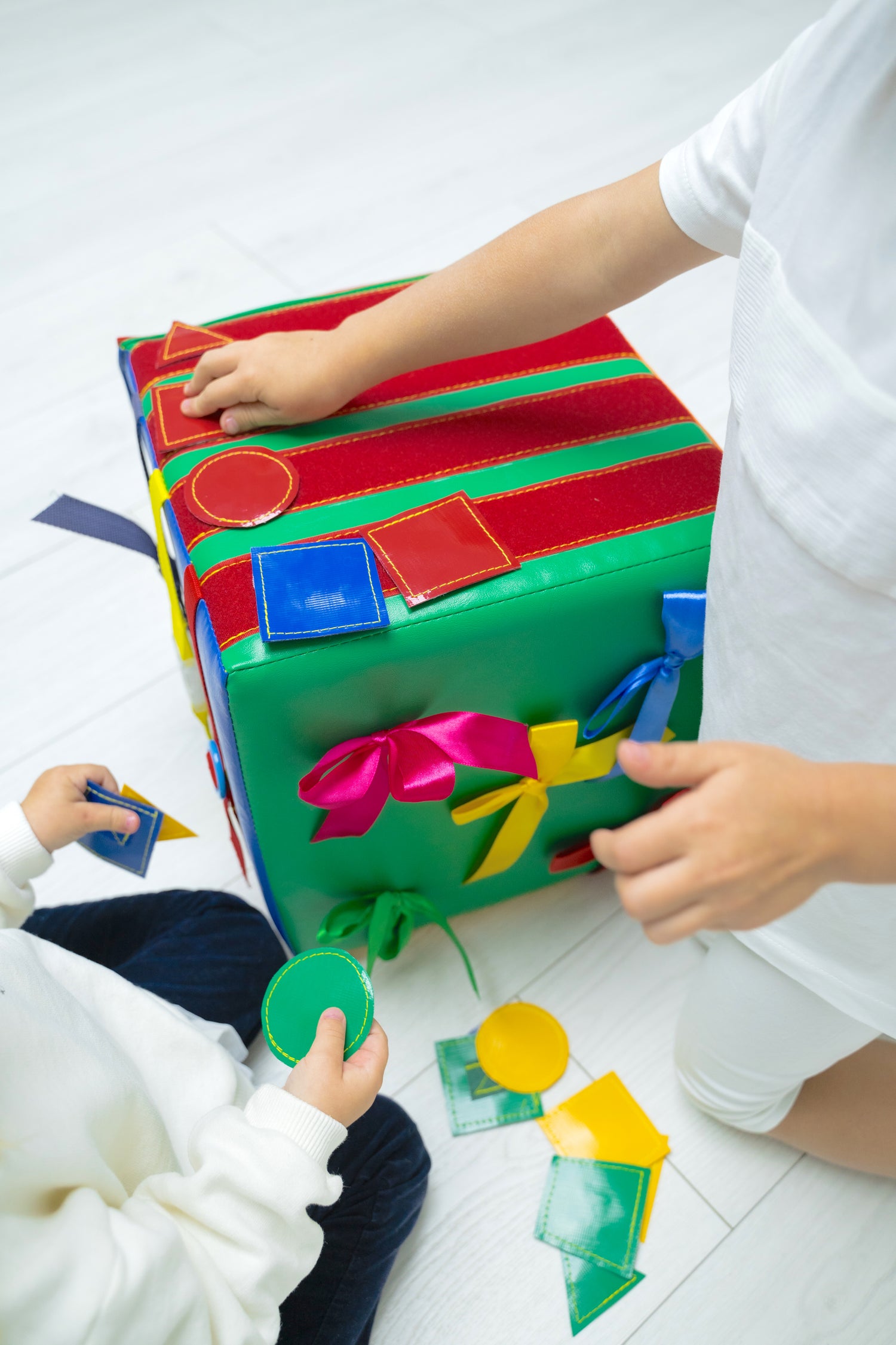Two young children playing with a large colourful felt quiet book/busy cube, shape sorter soft toy for toddlers' fine motor skills, Montessori educational play cube for kids' development
