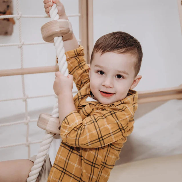 Child in a yellow plaid shirt climbing on a rope structure indoors