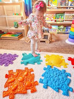 a toddler standing on sensory tactile mat which is in rainbow colour. There are 8 pieces in this set