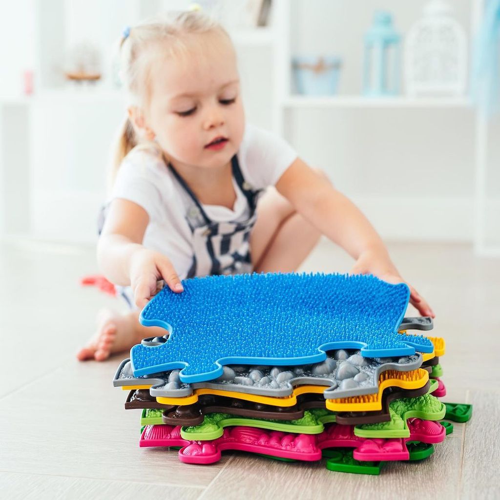 girl holding a set of sensory playmats by Tinnitots