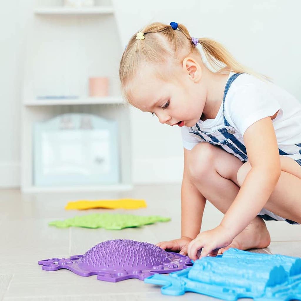 a girl exploring the textures of her purple hedgehog sensory mats for emotional regulation. sold by Tinnitots.