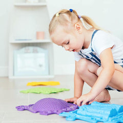 a girl exploring the textures of her purple hedgehog sensory mats for emotional regulation. sold by Tinnitots.